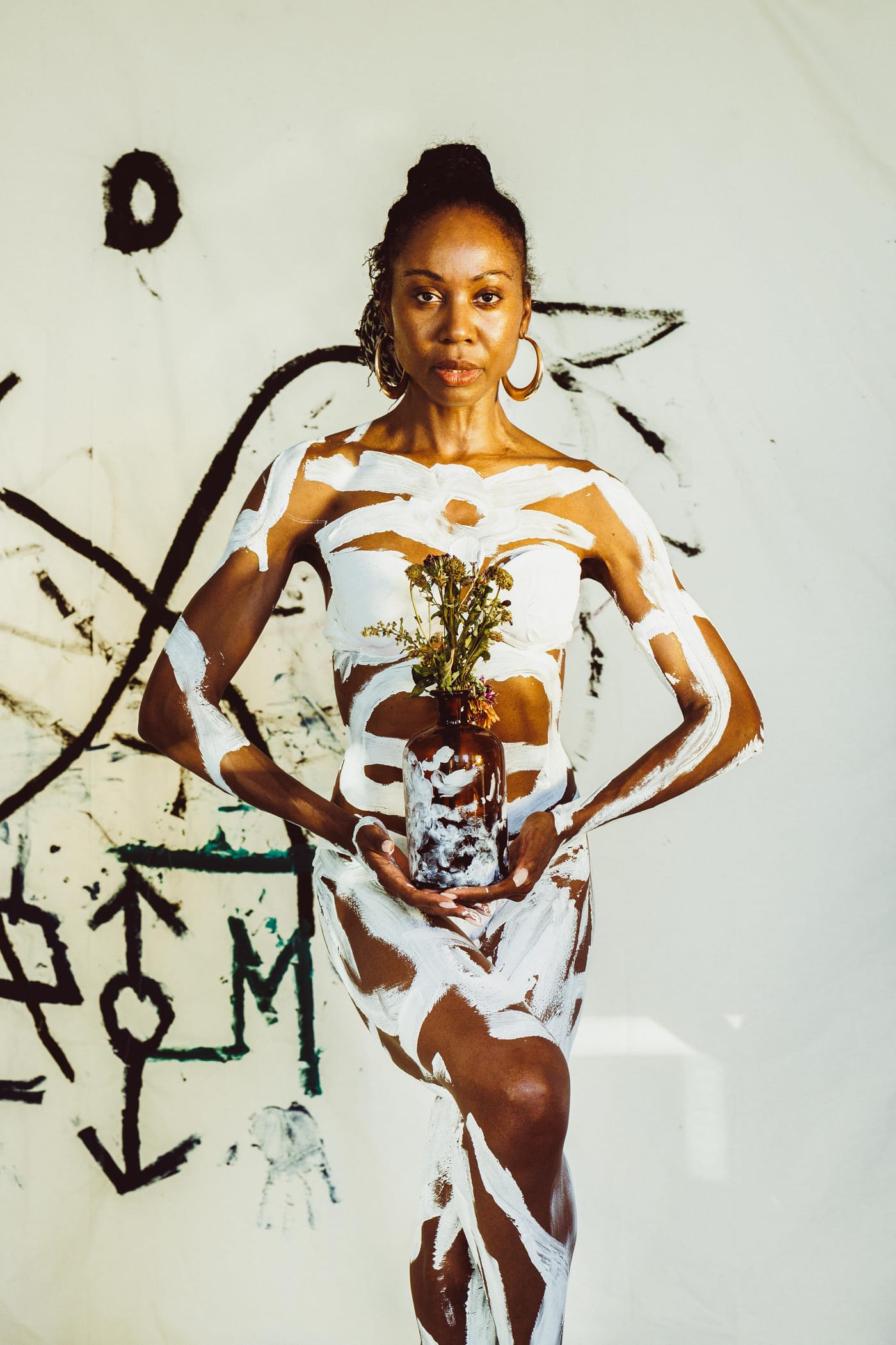 Figure in white and brown body paint against a marked wall