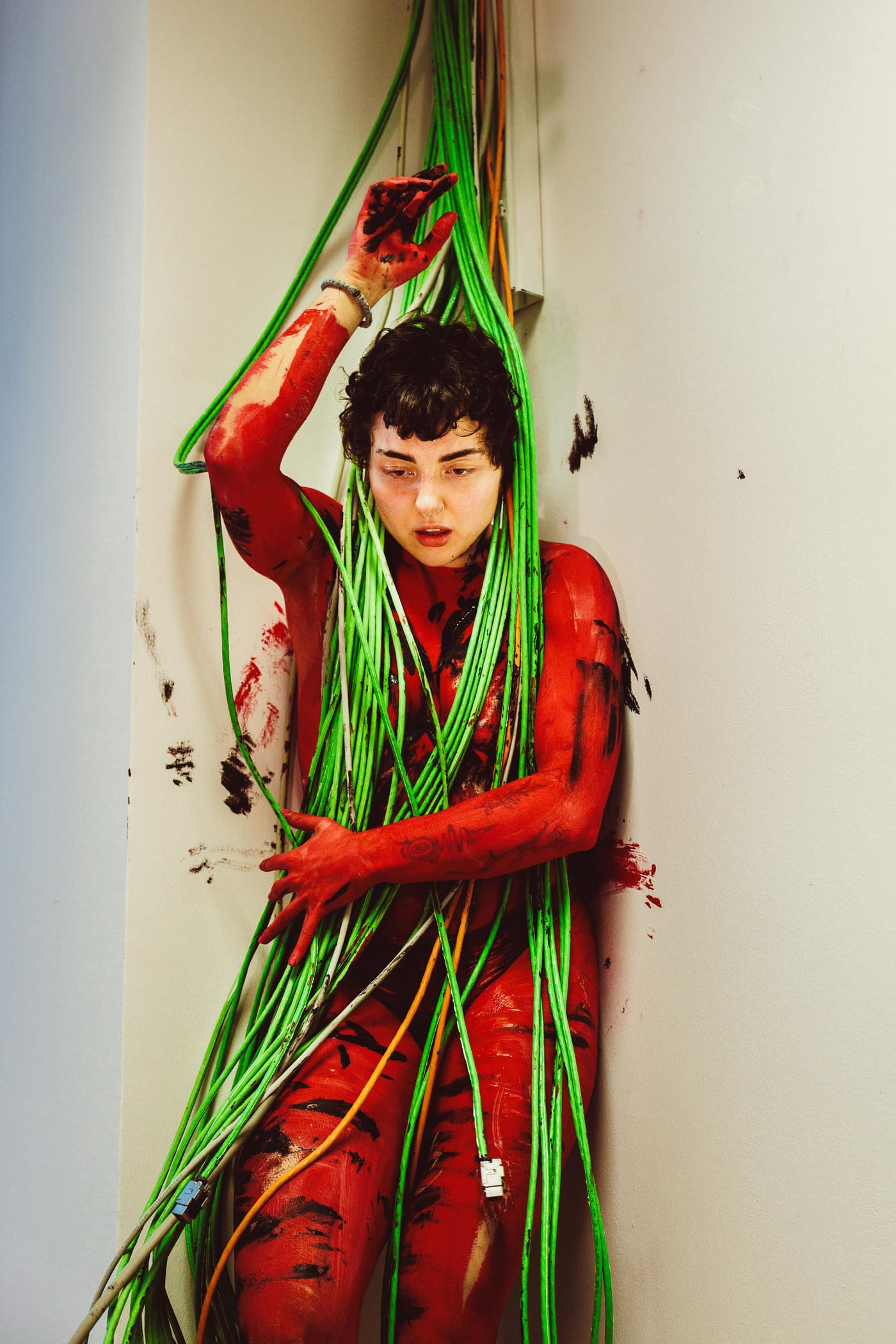 Figure wrapped in green cord against a red ground